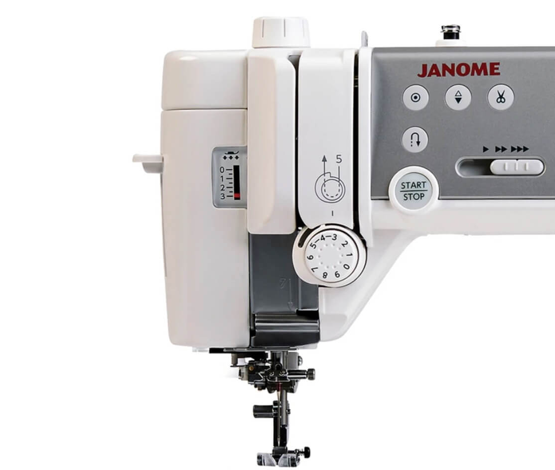Close-up view of the Janome Memory Craft 6700P's control panel and stitching area, highlighting the start/stop button, stitch selection dials, and detailed threading mechanism.